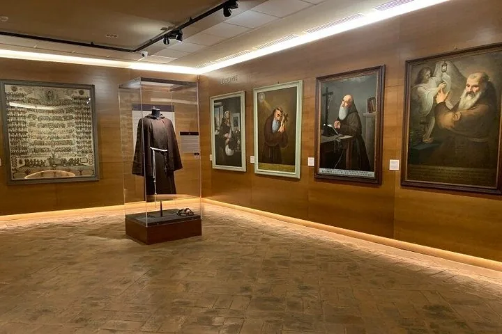 A well-lit museum room displaying religious paintings and a monk's robe in a case.
