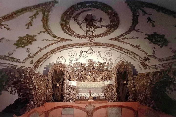 A wide view of a crypt room with bone-decorated walls, ceiling, and skeletal figures.
